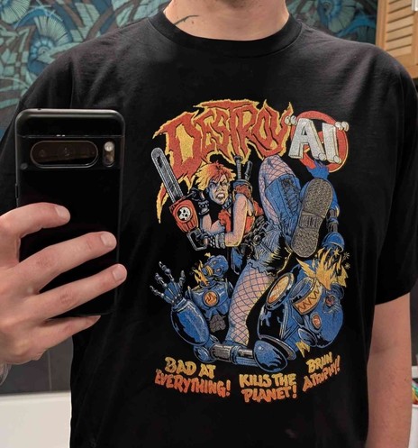 Selfie of me wearing a black shirt with a punk-looking woman wearing a chainsaw kicking down robots with the writing "DESTROY 'AI'" on top and "Bad at everything! Kills the Planet! Brain atrophy!" below.